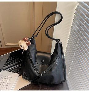 Detail of vintage black faux leather half-moon bag with grommet straps and bear charm
