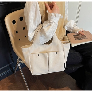 Detail of off-white canvas tote bag featuring metal snap buttons and spacious front pockets