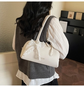 Back view of a model carrying the cream Boston bag with a delicate lace bow detail