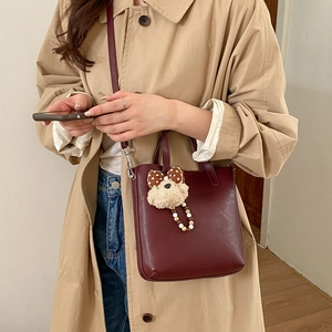 Détail du sac seau rouge foncé avec un charm ours en peluche et une bandoulière chic