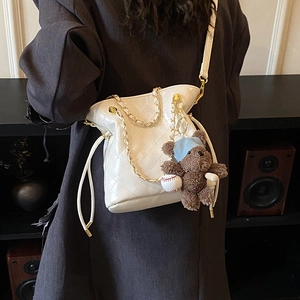 Detail of white quilted bucket bag with gold chain and plush bear charm on a model