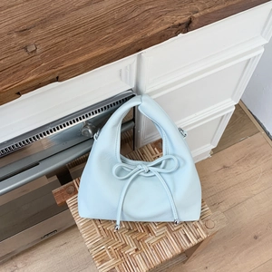 Close-up of sky blue bow handbag with lychee texture leather on wooden stool