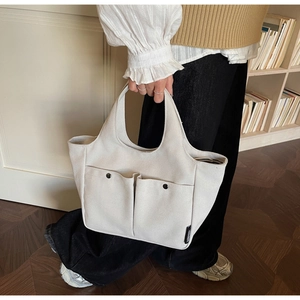 Detail of off-white canvas tote bag featuring metal snap pockets and side logo tag