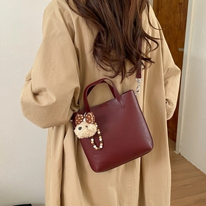 Vue détaillée d'un sac seau bordeaux avec un charme de chien en peluche sur un trench