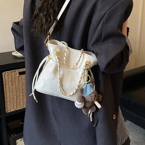 Detail view of white quilted bucket bag with gold chain strap and plush bear charm accent