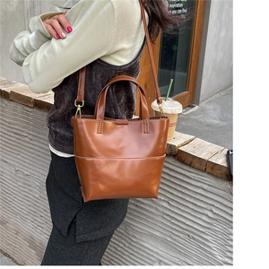 Borsa tote in pelle marrone con doppi manici e dettagli dorati indossata da una modella