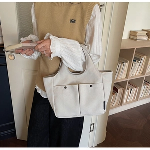 Detail of off-white canvas tote bag with front pockets shown in a daily life scene