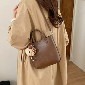 Vue détaillée du sac seau marron foncé avec charm ours en peluche et bandoulière amovible
