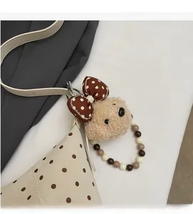 Detail of a beige teddy bear plush charm with polka dot bow on a minimalist bag