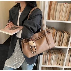 Detail of vintage khaki tote bag with textured leather and cute plush bear charm on a shoulder strap
