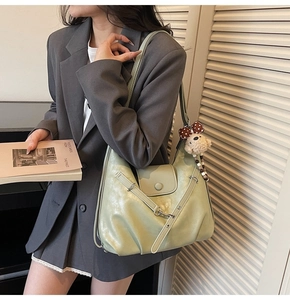 Detail of light green glossy leather shoulder bag with cute plush bear charm in soft lighting