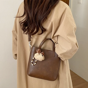 Sac seau en similicuir marron foncé porté en bandoulière avec un charmant ours en peluche