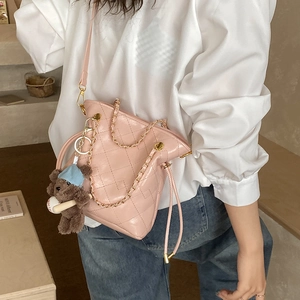 Detail of pink quilted bucket bag with golden chain strap and plush bear charm decoration