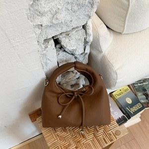 Detail view of the brown leather bag featuring a unique knotted handle and decorative bow