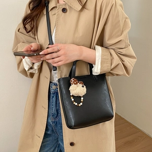 Détail du sac seau noir en cuir avec breloque ours en peluche et bandoulière fine