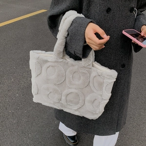 Detailed view of grey faux fur tote bag with circular 3D pattern held by a model