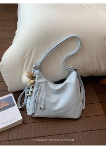 Light blue hobo shoulder bag with fuzzy keychain on wooden floor home setting