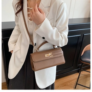 Detailed view of brown lychee texture leather bag with gold metal lock on a white blazer