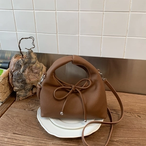 Detailed shot of brown PU handbag with bow decoration and silver metal buckles on a white plate