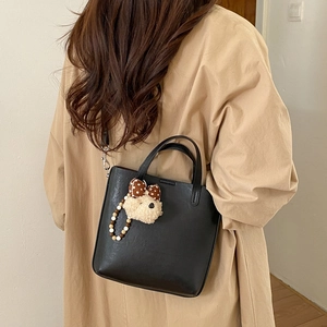 Détail d'un sac seau en cuir noir minimaliste avec un pendentif ours en peluche mignon