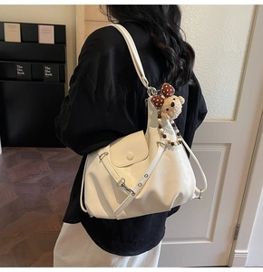 Detail of cream white faux leather bag with vintage metal buckle and plush bear charm