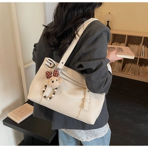 Close-up of off-white pebble leather tote bag with cute plush bear charm for daily commute