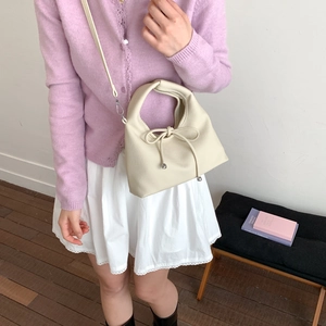 Close-up of cream-colored dumpling bag with leather bow detail on purple cardigan