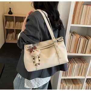 Detail of creamy white pebble leather tote bag with a cute plush bear charm on shoulder