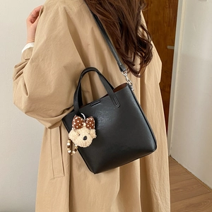 Détail du sac seau en cuir noir avec breloque d'ours en peluche et bandoulière