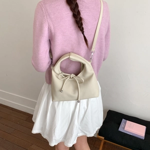 Detail view of cream dumpling bag with ribbon bow on model with pink sweater