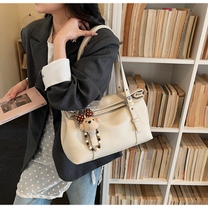 Detail of off-white lychee grain tote bag with bear charm worn by a model in a library