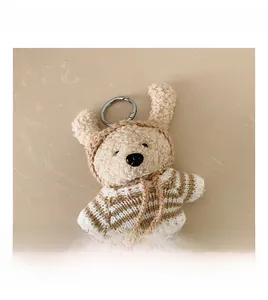 Detail view of a teddy bear plush pendant with striped sweater and silver metal keychain