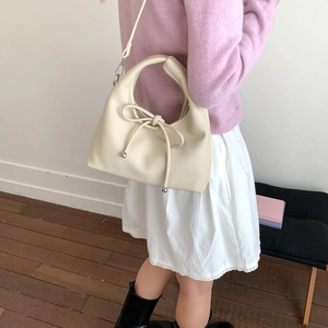 Detail of cream pleated crossbody bag with bow tie and silver ball charm on model