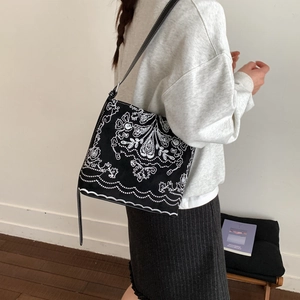 Sac seau rétro noir avec broderie florale blanche et bordure ondulée élégante