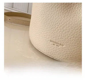 Detailed macro view of cream pebbled leather bucket bag with embossed logo and thin strap