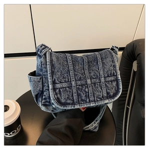Detailed close-up of dark blue washed denim shoulder bag with stitching and side pocket