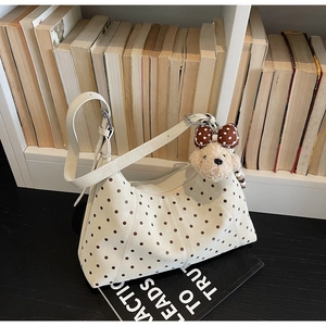 Detailed view of cream polka dot shoulder bag with brown bear plush charm and zipper detail