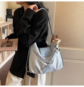 Detail of light blue leather bag with cross-straps and a cute brown bear charm