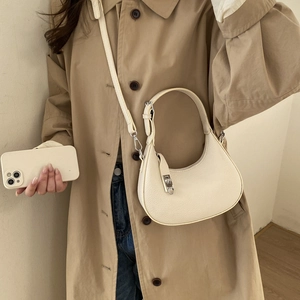 Détail d'un sac demi-lune crème porté sur un trench-coat beige élégant en gros plan
