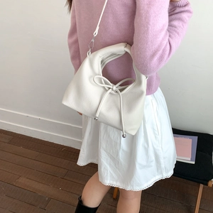 Detail of off-white dumpling bag with a delicate bow and metallic bottom studs