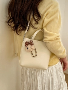 Sac seau beige avec breloque d'ours porté par un mannequin pour un style décontracté