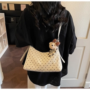 Close-up of white polka dot shoulder bag with cute plush bear charm on a model