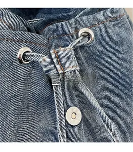 Detail of blue denim backpack showing metal eyelets, drawstring and magnetic snap closure
