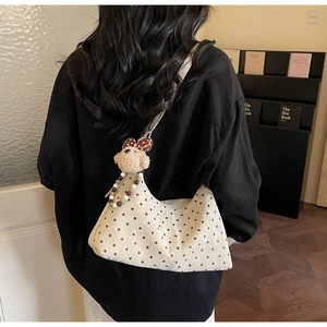 Polka dot crossbody bag with plush bear charm worn by a model in an indoor setting