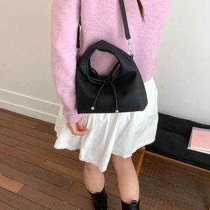 Crossbody view of a black leather dumpling bag with long bow detail on model