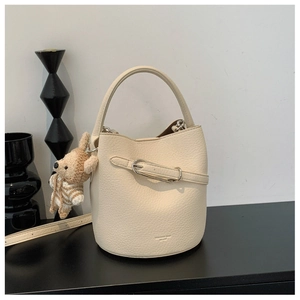 Close-up of creamy white lychee leather bucket bag with cute bear charm and gold buckle