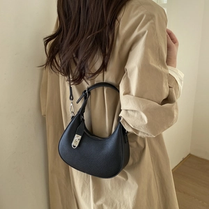 Détail d'un sac hobo en cuir noir avec boucle argentée porté sur un trench beige
