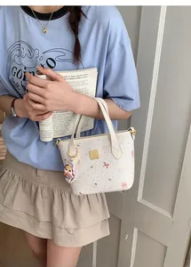 Dettaglio della borsa a secchiello bianca con stampe di gatti rosa e charm in peluche