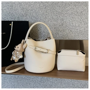 Detail view of cream bucket bag with lychee texture, matching pouch and cute bear pendant