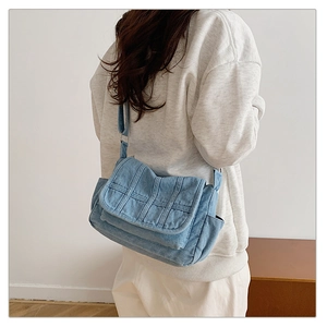 Detail of light blue denim crossbody bag featuring vertical stitching and side pocket